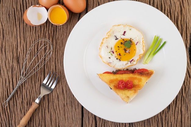 Spiegelei auf einem weißen Teller mit Toast, geschnittenen Frühlingszwiebeln und geschnittenen Tomaten