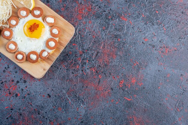 Spiegelei serviert mit gegrillter Wurst und Gewürzen auf einer Holzplatte.