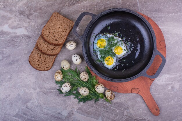 Spiegeleier in einer Metallpfanne mit Brotscheiben.