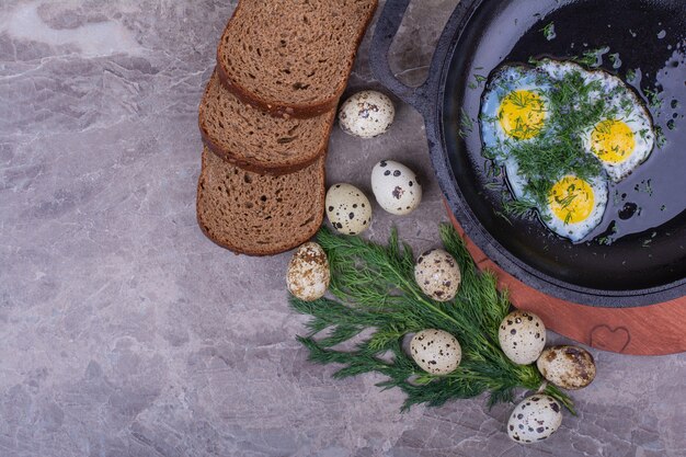 Spiegeleier in einer schwarzen Pfanne mit Kräutern und Brot