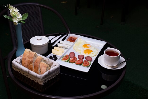 Spiegeleier mit Würstchen, Oliven, Käse, Brot und einer Tasse Tee