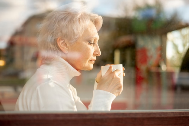 Kostenloses Foto spiegelung des weiblichen älteren trinkenden kaffees