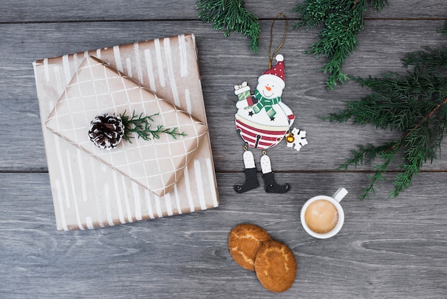 Spielen Sie Schneemann nahe Geschenken in den Verpackungen mit Baumstumpf, Zweigen, Cup des Getränks und Plätzchen