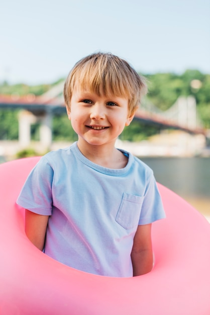 Spielerischer Junge, der mit Schwimmring auf Ufer steht