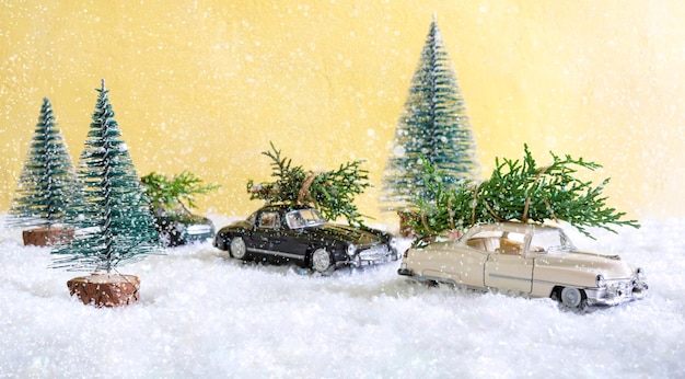 Spielzeugautos im wald zwischen den schneeverwehungen liefern weihnachtsbäume. unscharfer hintergrund. magische atmosphäre, konzept der weihnachtsferien. grußkarte.