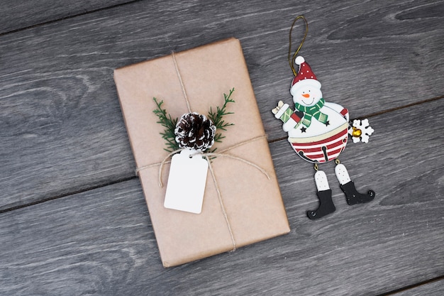 Spielzeugschneemann nahe Geschenk in der Verpackung mit Baumstumpf und Tag