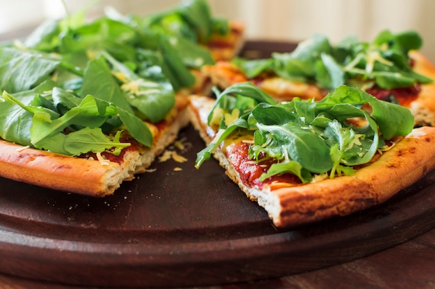 Spinatspitzen auf der Scheibe der Pizza über hölzernem Behälter