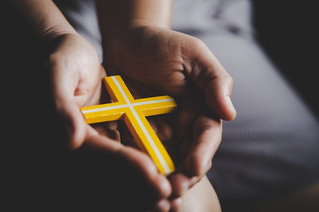 Kostenloses Foto spiritualität und religion, frauen in religiösen konzepten hände, die zu gott beim halten des kreuzsymbols beten. nun fing das kreuz in seiner hand auf.