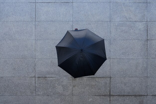 Spitzenschuß der unerkennbaren Person stehend unter Regenschirm auf Pflasterung