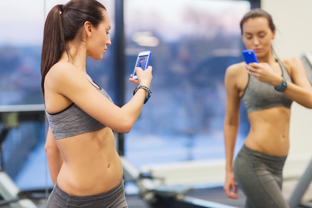 Sport-, fitness-, lebensstil-, technologie- und personenkonzept - junge frau mit smartphone, das spiegel-selfie im fitnessstudio nimmt