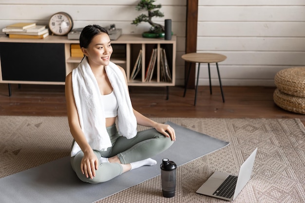 Sport- und lifestyle-konzept lächelnde junge asiatische frau, die zu hause yoga macht, folgen dem meditationskurs auf...