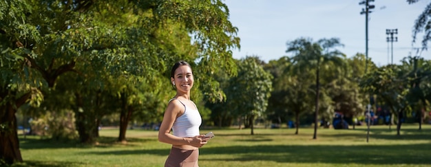 Kostenloses Foto sport und wohlbefinden junge sportlerin im park hört musik und lächelt und trainiert im freien beim joggen