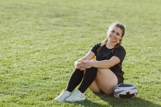 Sportive Frau, die auf Gras nahe bei einer Kugel sitzt