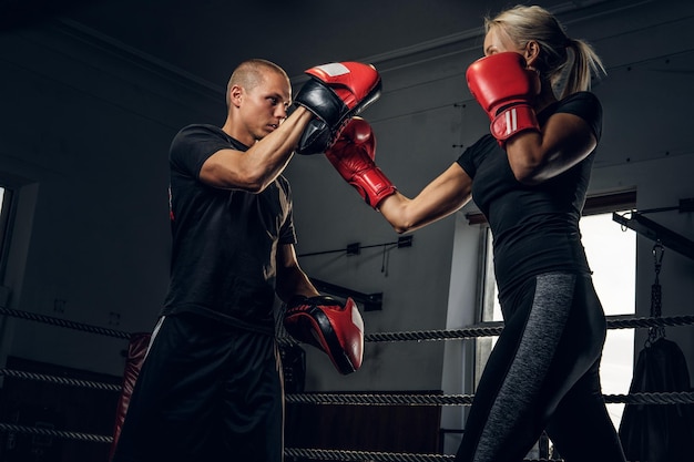 Sportliche blonde Frau hat Boxtraining mit ihrem erfahrenen Trainer.