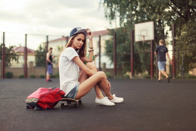 Sportliche Frau auf Skateboard sitzt im Freien