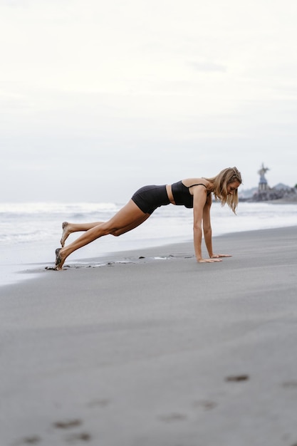 Sportliche Frau, die Bergsteigerübungen macht - in Planke laufen, um Fett zu verbrennen. Sunset Beach, Hintergrund des blauen Himmels. Gesunder Lebensstil im tropischen Insel-Yoga-Retreat, Outdoor-Aktivitäten, Sommerurlaub mit der Familie.