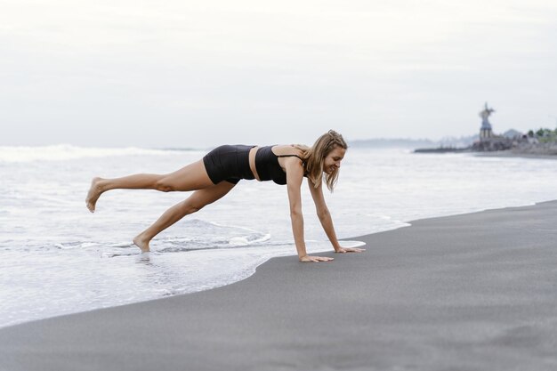 Sportliche Frau, die Bergsteigerübungen macht - in Planke laufen, um Fett zu verbrennen. Sunset Beach, Hintergrund des blauen Himmels. Gesunder Lebensstil im tropischen Insel-Yoga-Retreat, Outdoor-Aktivitäten, Sommerurlaub mit der Familie.