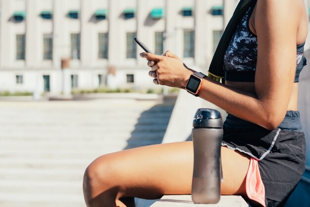 Sportliche Frau, die ihr Handy benutzt und sich nach dem Training im Freien entspannt. Sport und gesunder Lebensstil.