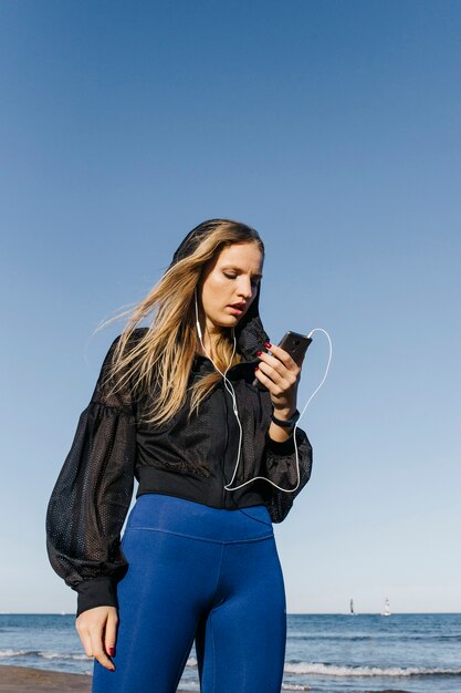 Sportliche Frau, die Smartphone auf den Strand betrachtet