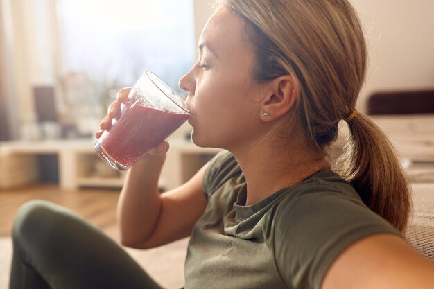 Sportliche Frau genießt zu Hause ein Glas frischen Fruchtsmoothie