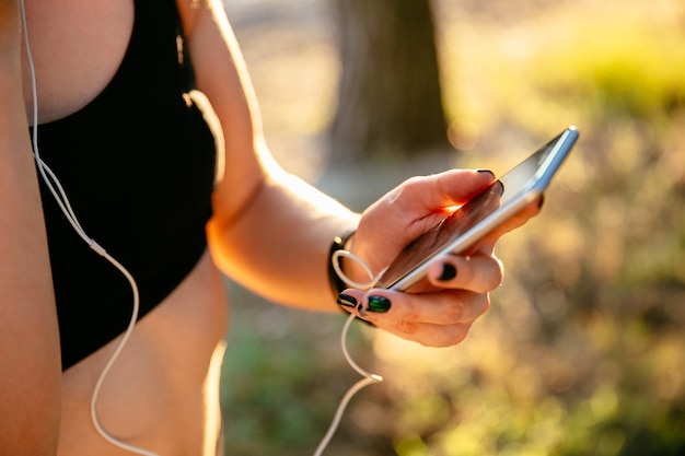 sportliche Frau im schwarzen Trägershirt unter Verwendung eines Handys beim Hören Musik