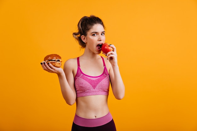 Kostenloses Foto sportliche frau isst roten apfel auf orange wand