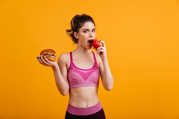 Sportliche Frau isst roten Apfel auf orange Wand