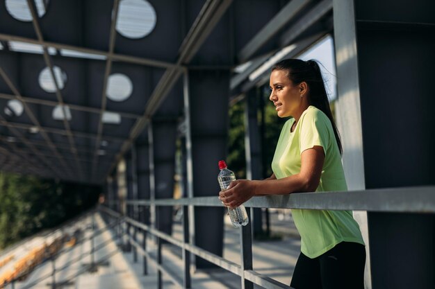 Sportliche Frau mit Flasche Wasser, die sich nach dem Training ausruht