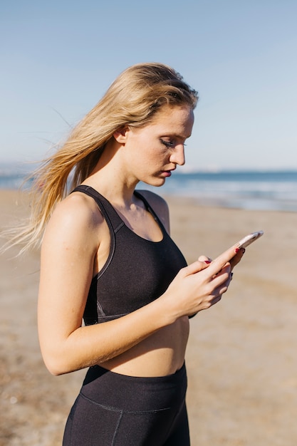 Sportliche Frau mit Smartphone am Strand