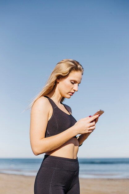Sportliche Frau mit Smartphone am Strand