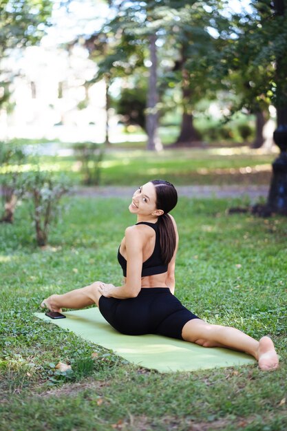 Sportliche junge Frau, die morgens im Park Yoga macht, Frauentraining auf einer Yogamatte