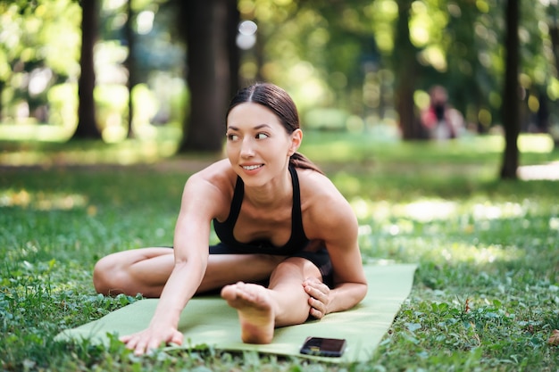 Sportliche junge Frau, die Yoga im Park am Morgen tut.