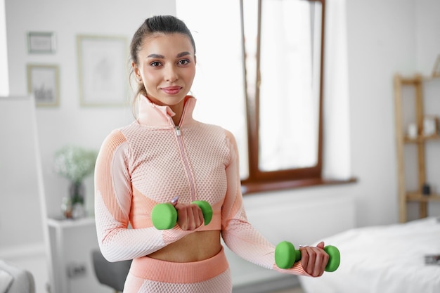 Sportliche junge Frau, die zu Hause mit Hanteln trainiert