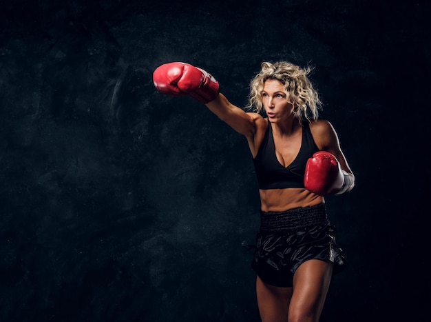 Sportliche muskulöse Frau demonstriert ihre Boxübungen und trägt Handschuhe.