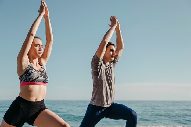 Sportliche Paare, die Yoga am Strand tun