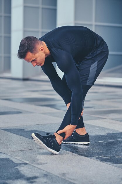 Sportlicher, athletischer Mann wärmt sich auf und streckt sich im Freien über modernem Gebäudehintergrund.