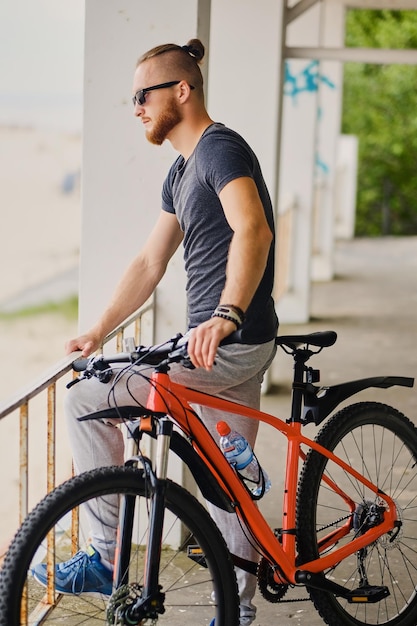 Sportlicher bärtiger Mann sitzt auf einem roten Mountainbike im Freien.