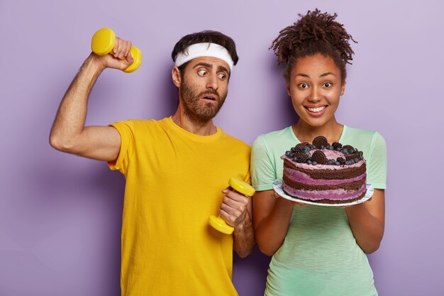 Sportlicher gesunder Lebensstil gegen Junk Food. Verwirrter Sportler hält Hanteln