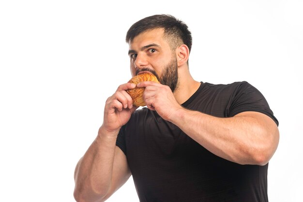 Sportlicher Mann im schwarzen Hemd, der einen Donut isst.