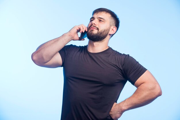 Sportlicher Mann im schwarzen Hemd hält das Telefon und spricht