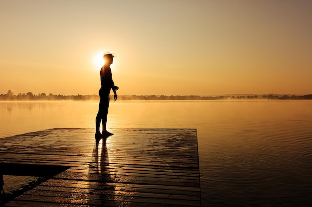 Sportlicher Mann in Silhouette, der sich nach dem morgendlichen Schwimmen am Pier entspannt