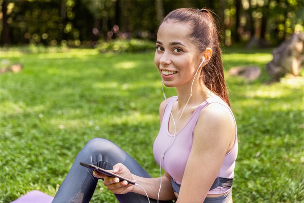 Sportliches Mädchen, das auf einer Yogamatte und einer hörenden Musik sitzt