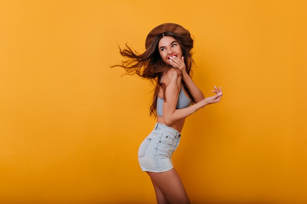 Sportliches Mädchen, das Mund mit Hand während Fotoshooting auf gelbem Raum bedeckt