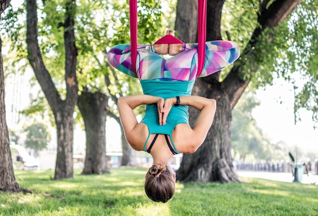 Sportmädchen, das fliegenyoga in der hängematte in der natur praktiziert und ihren körper ausdehnt. sportlerin bei aero-gymnastik im freien