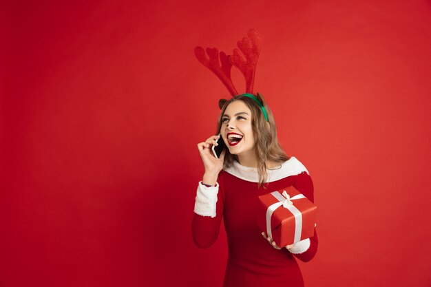 Sprechendes Telefon mit Geschenk. Konzept von Weihnachten, Neujahr, Winterstimmung, Feiertagen. Schöne kaukasische Frau mit langen Haaren wie Santa's Rentier anziehende Geschenkbox.