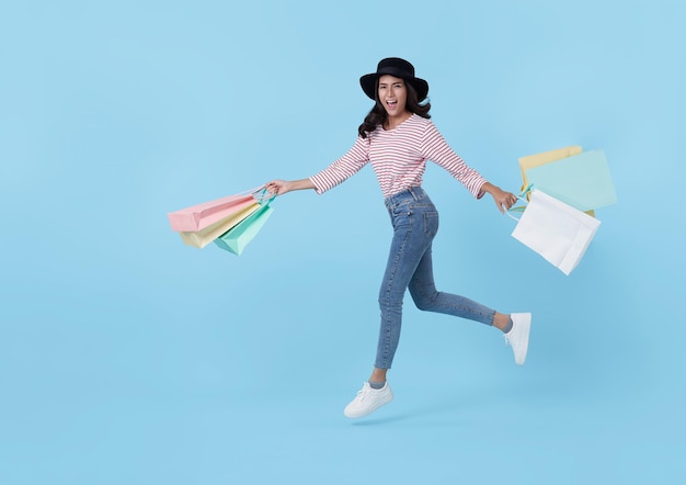 Springende glückliche jugendlich asiatische Frau, die das Einkaufen genießt, sie trägt Einkaufstaschen