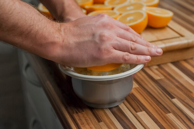 Squeezing Orangen, um einen frischen und natürlichen Saft zu machen. Closeup auf Mann machen frischen Orangensaft. Orangen und Saftpresse auf dem Holzbrett