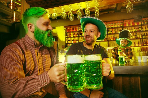 St. Patrick's Day Party. Glückliche Freunde feiern und trinken grünes Bier. Junge Männer und Frauen tragen grüne Hüte. Pub Interieur.