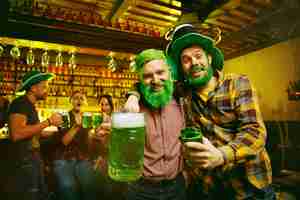 Kostenloses Foto st. patrick's day party. glückliche freunde feiern und trinken grünes bier. junge männer und frauen tragen grüne hüte. pub interieur.