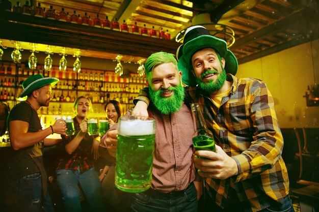 St. Patrick's Day Party. Glückliche Freunde feiern und trinken grünes Bier. Junge Männer und Frauen tragen grüne Hüte. Pub Interieur.